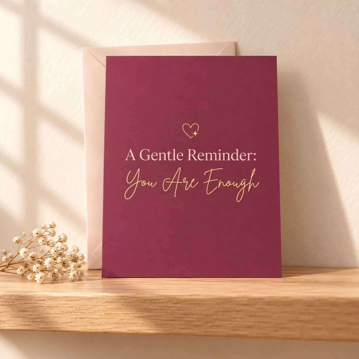 A Gentle Reminder: You Are Enough card in warm berry with a small gold heart, standing on a light oak shelf beside dried baby's breath