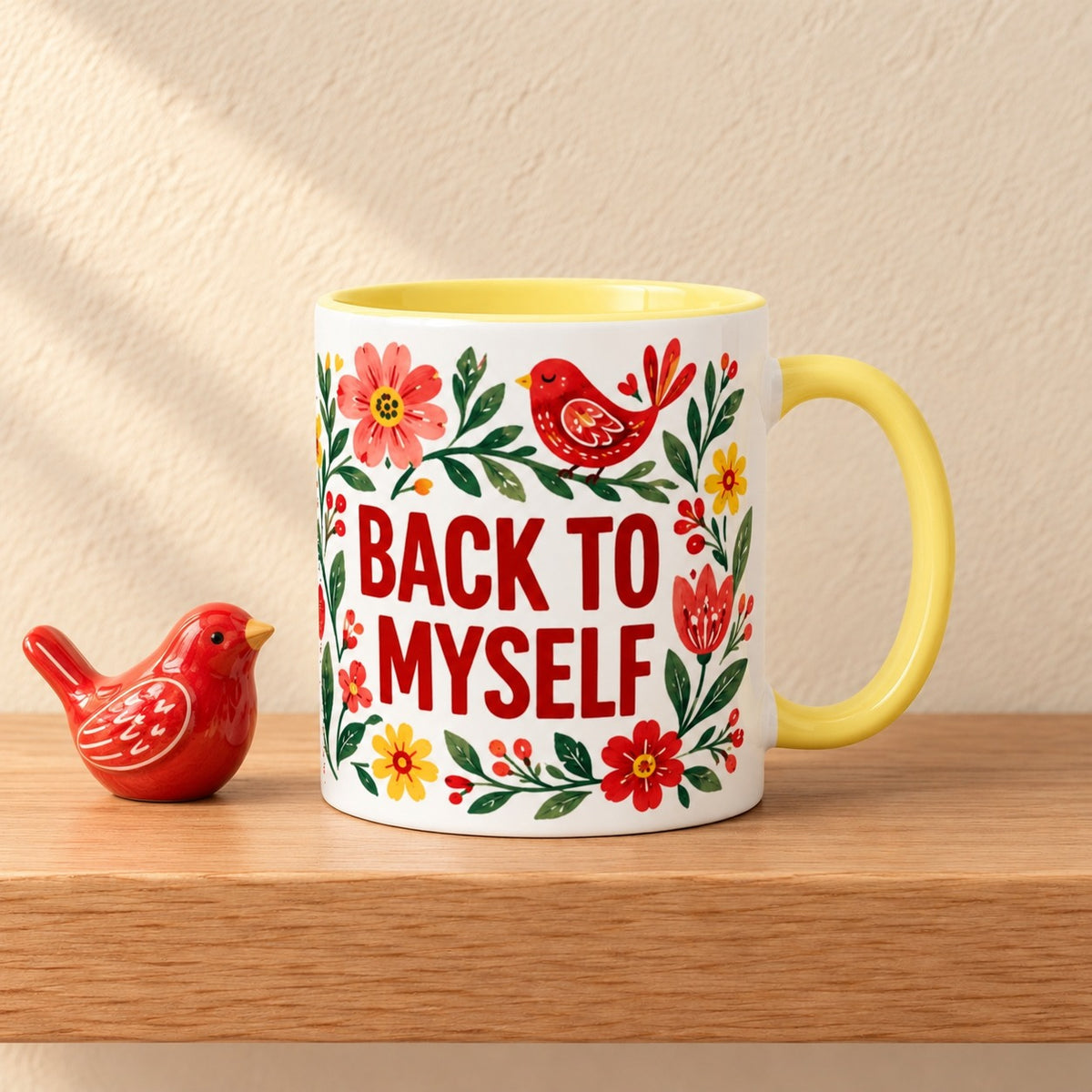 Back to Myself 11 oz mug with a yellow handle and yellow inside, title facing forward among folk art flowers and a red bird, resting on a light oak shelf beside a small red ceramic bird