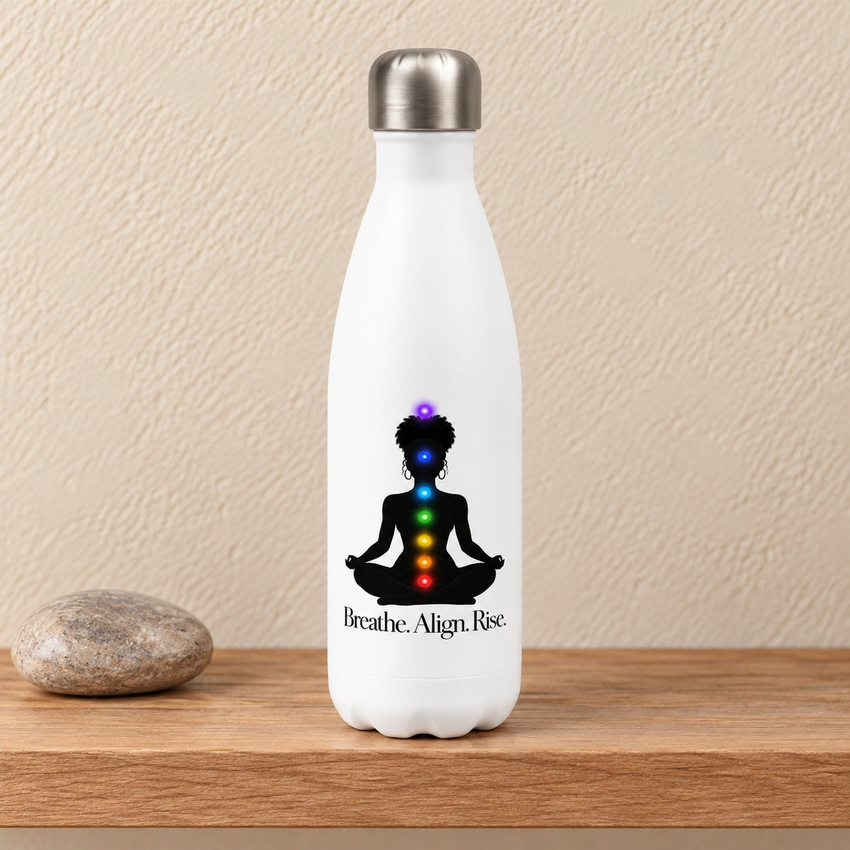Breathe. Align. Rise. 17 oz white water bottle with a meditating woman silhouette and chakra lights, standing on a light oak shelf beside a river stone