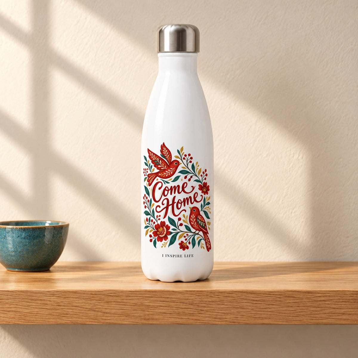 Come Home 17 oz white stainless steel water bottle on a light oak shelf beside a small teal ceramic bowl, design facing forward