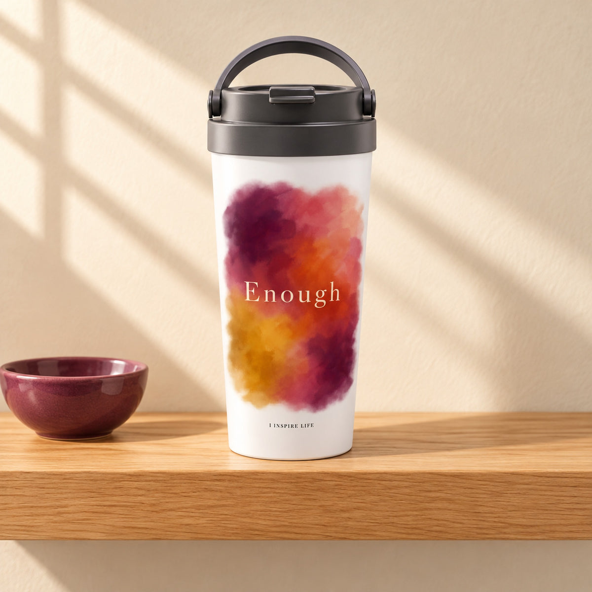 Enough 15 oz white stainless steel travel mug on a light oak shelf beside a small plum ceramic bowl, design facing forward