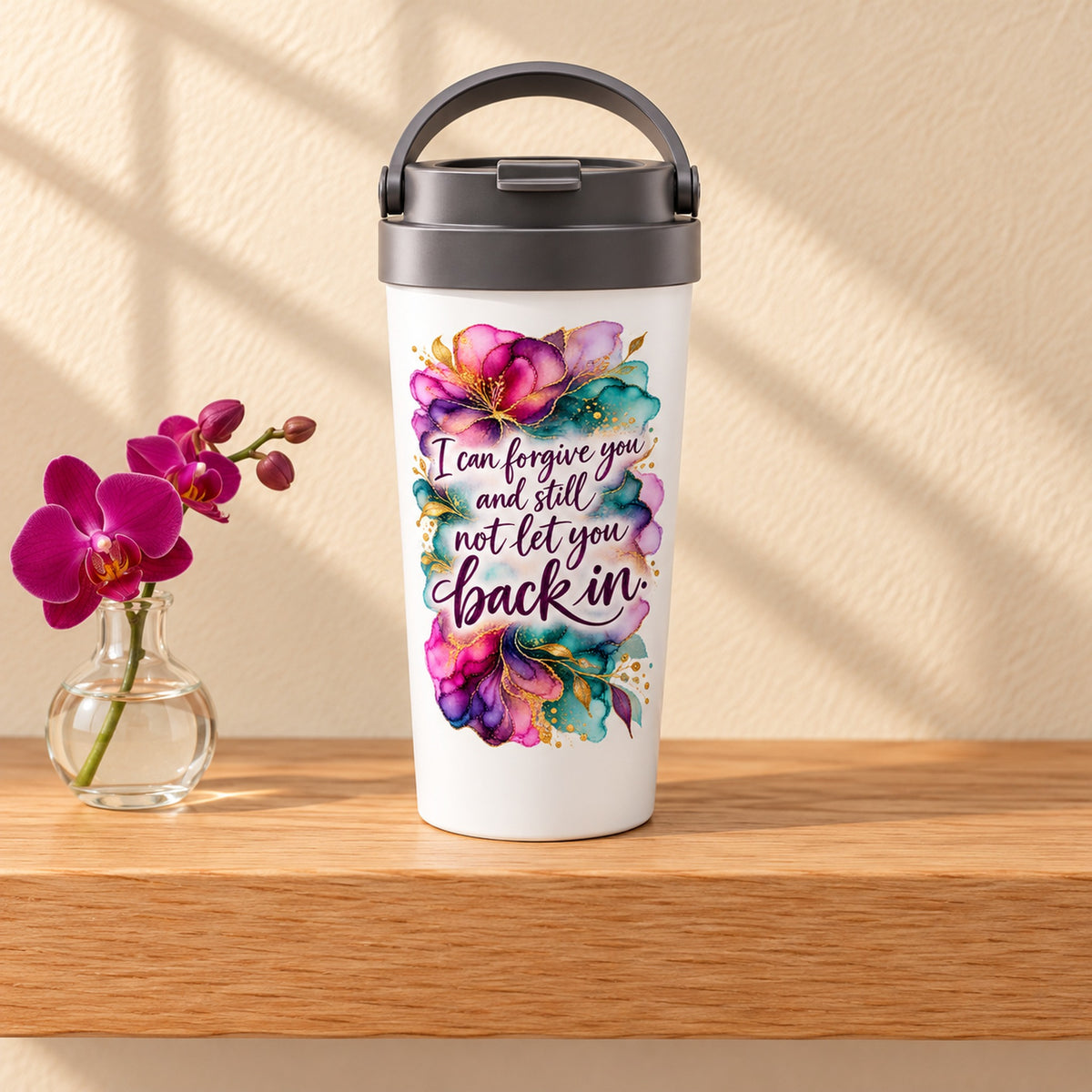 Forgive, Not Return 15 oz white stainless steel travel mug on a light oak shelf beside a magenta orchid, design facing forward