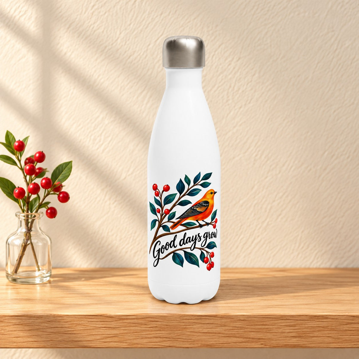 Good Days Grow white 17 oz water bottle with an orange folk art songbird on a berry branch, standing on a light oak shelf beside red berries in a glass bottle