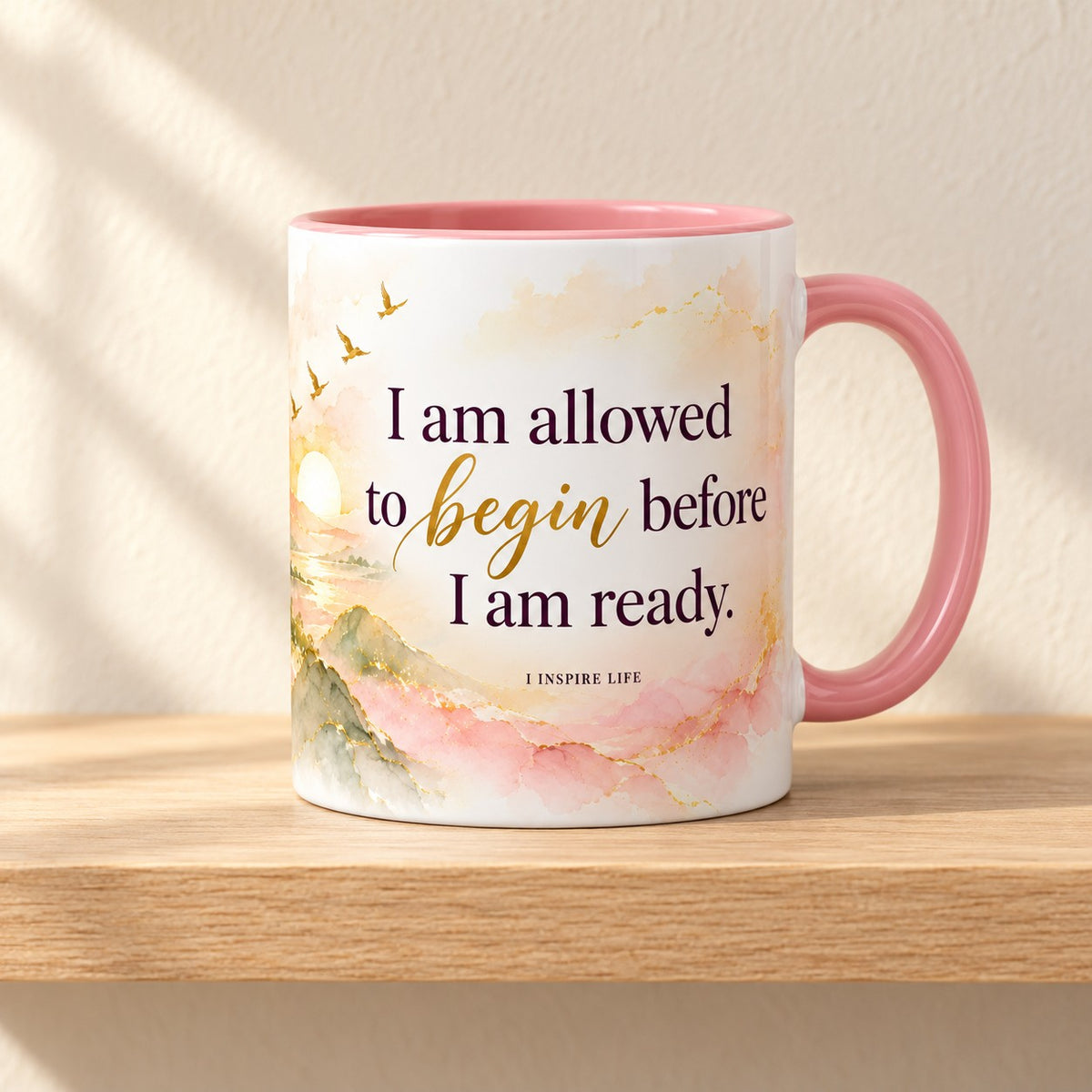 I Am Allowed to Begin 11 oz mug with a pink handle, the statement facing forward over an alcohol ink sunrise, resting on a light oak shelf