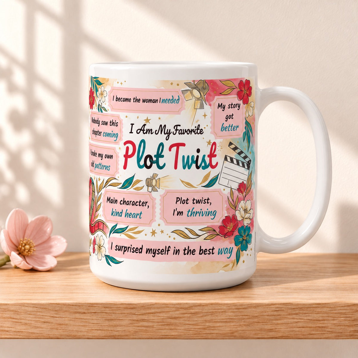 I Am My Favorite Plot Twist 15 oz white mug with the title facing forward, resting on a light oak shelf beside a small pink flower