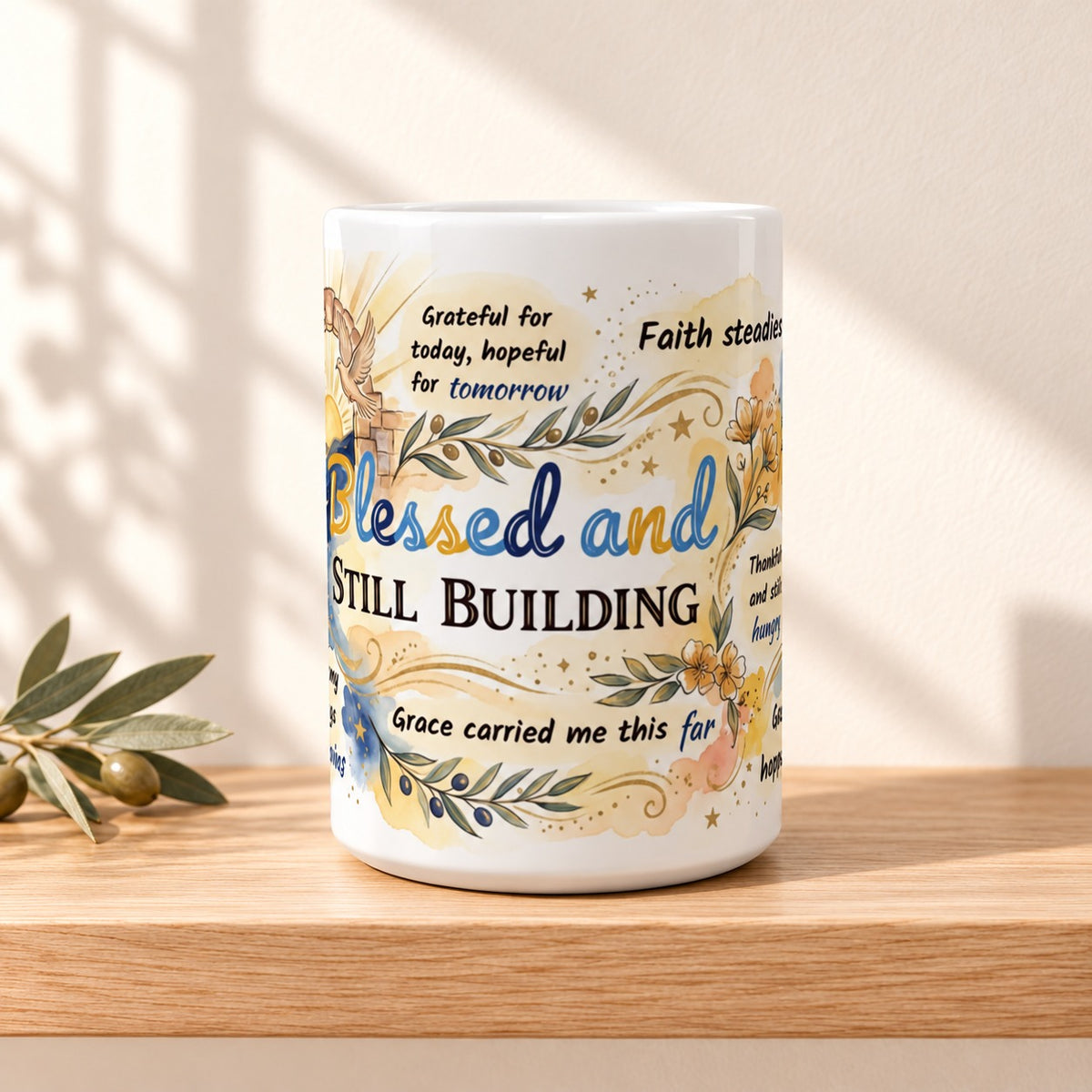 Blessed and Still Building 15 oz white ceramic mug resting on a light oak shelf against a warm cream wall