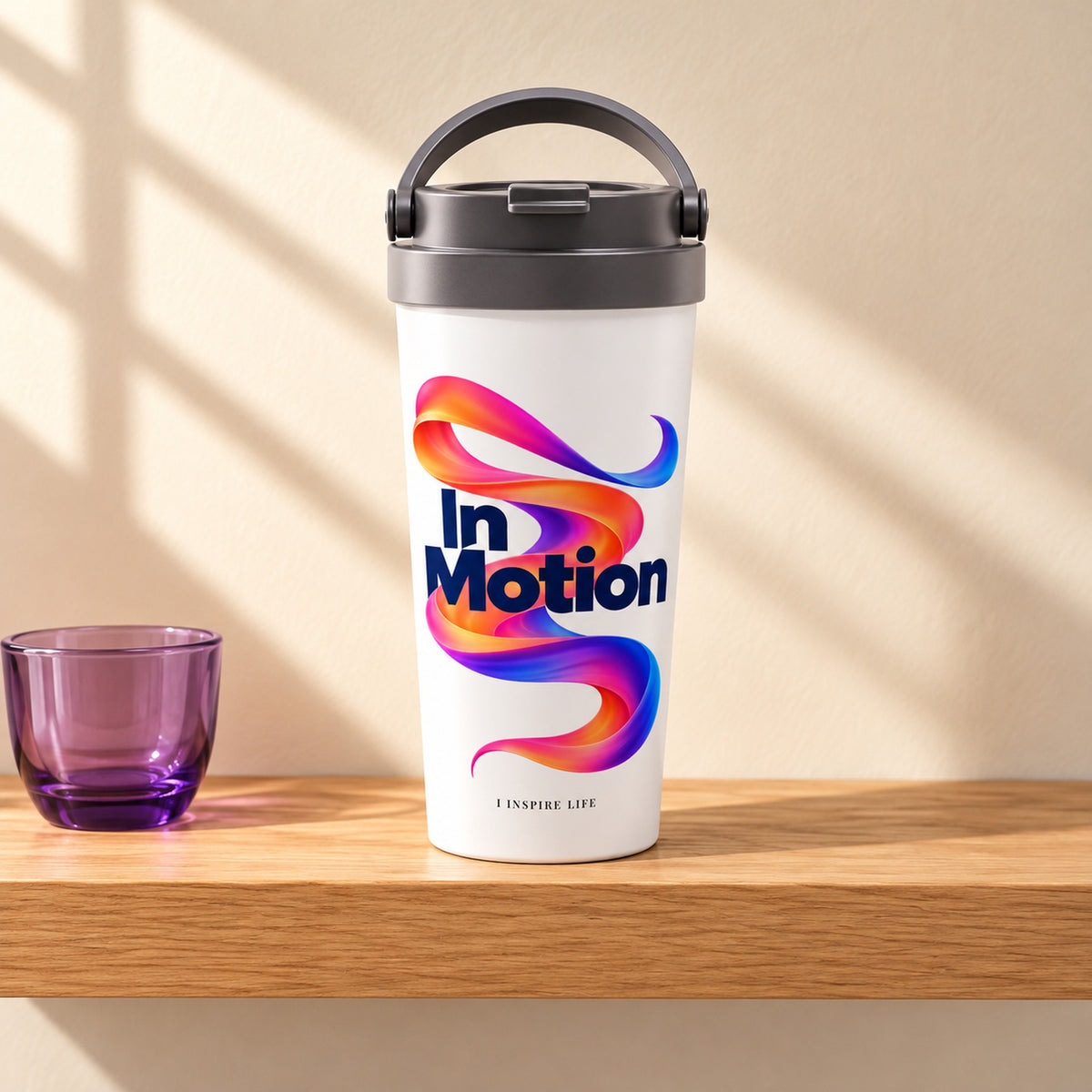 In Motion 15 oz white stainless steel travel mug on a light oak shelf beside a small violet glass cup, design facing forward