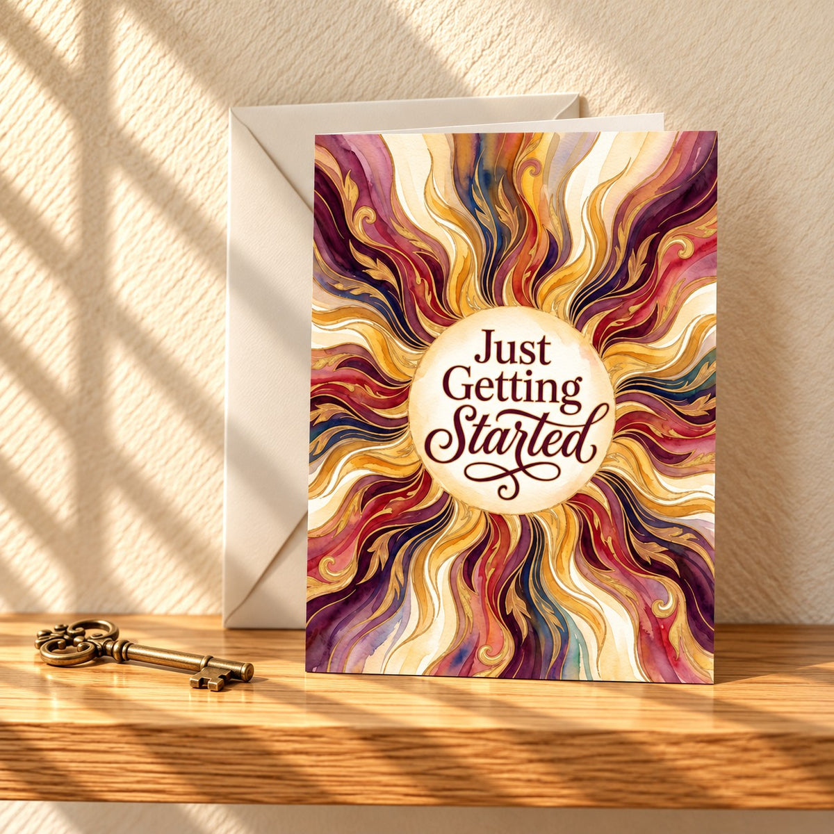 Just Getting Started card with a swirling burgundy and gold marbled sunburst, standing on a light oak shelf beside an antique brass key