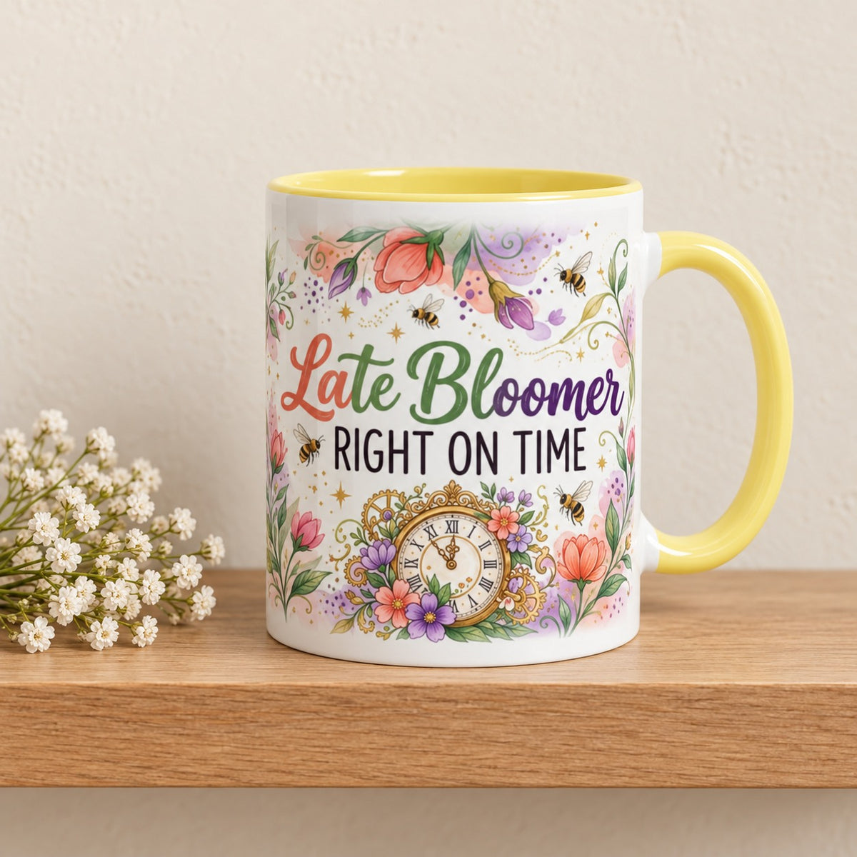 Late Bloomer Right on Time 11 oz mug with a yellow handle and yellow inside, title facing forward, resting on a light oak shelf beside a sprig of baby's breath