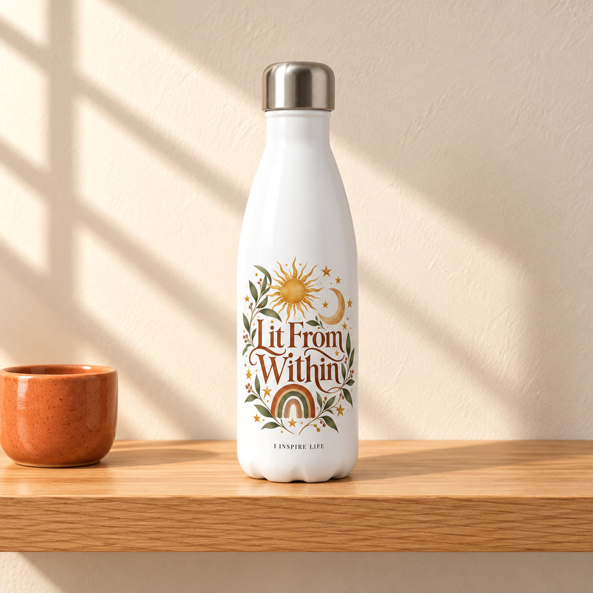 Lit From Within 17 oz white stainless steel water bottle on a light oak shelf beside a small terracotta ceramic cup, design facing forward