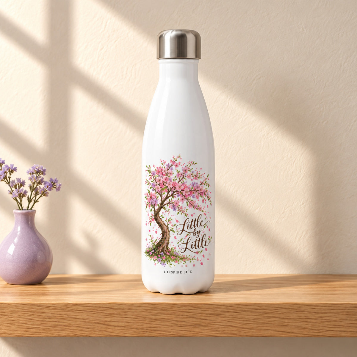 Little by Little 17 oz white stainless steel water bottle on a light oak shelf beside a small lilac ceramic bud vase, design facing forward