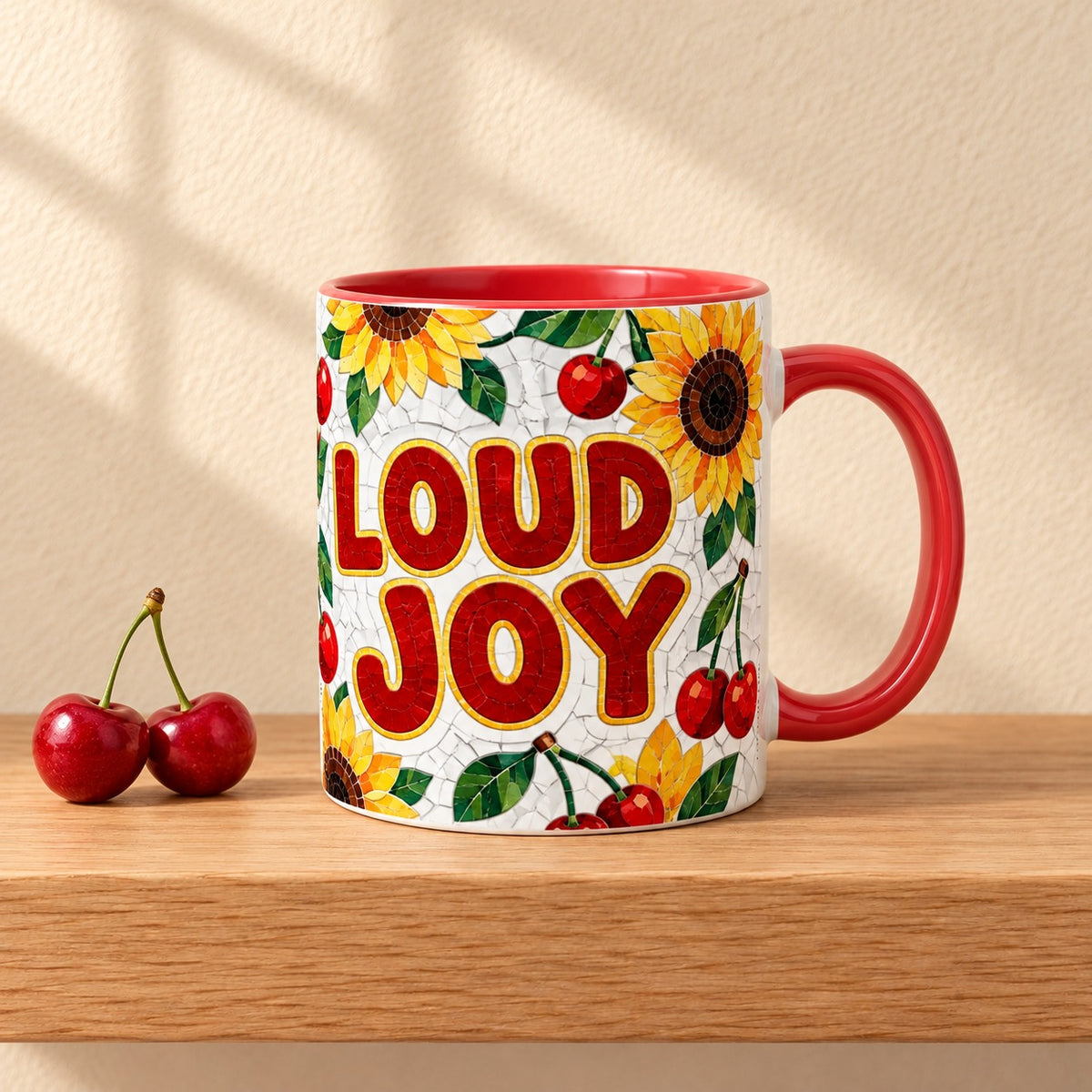 Loud Joy 11 oz mug with a red handle and red inside, title facing forward among sunflowers and cherries, resting on a light oak shelf beside two fresh cherries
