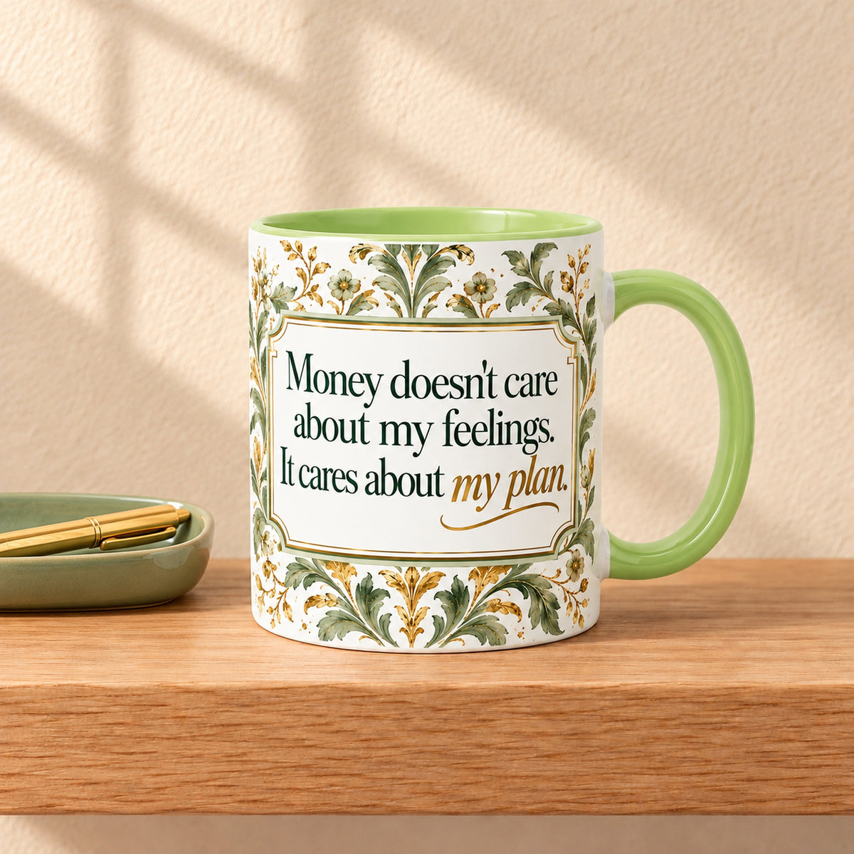 Money Doesn't Care 11 oz ceramic mug with a green handle on a light oak shelf beside a sage tray and gold pen, title facing forward