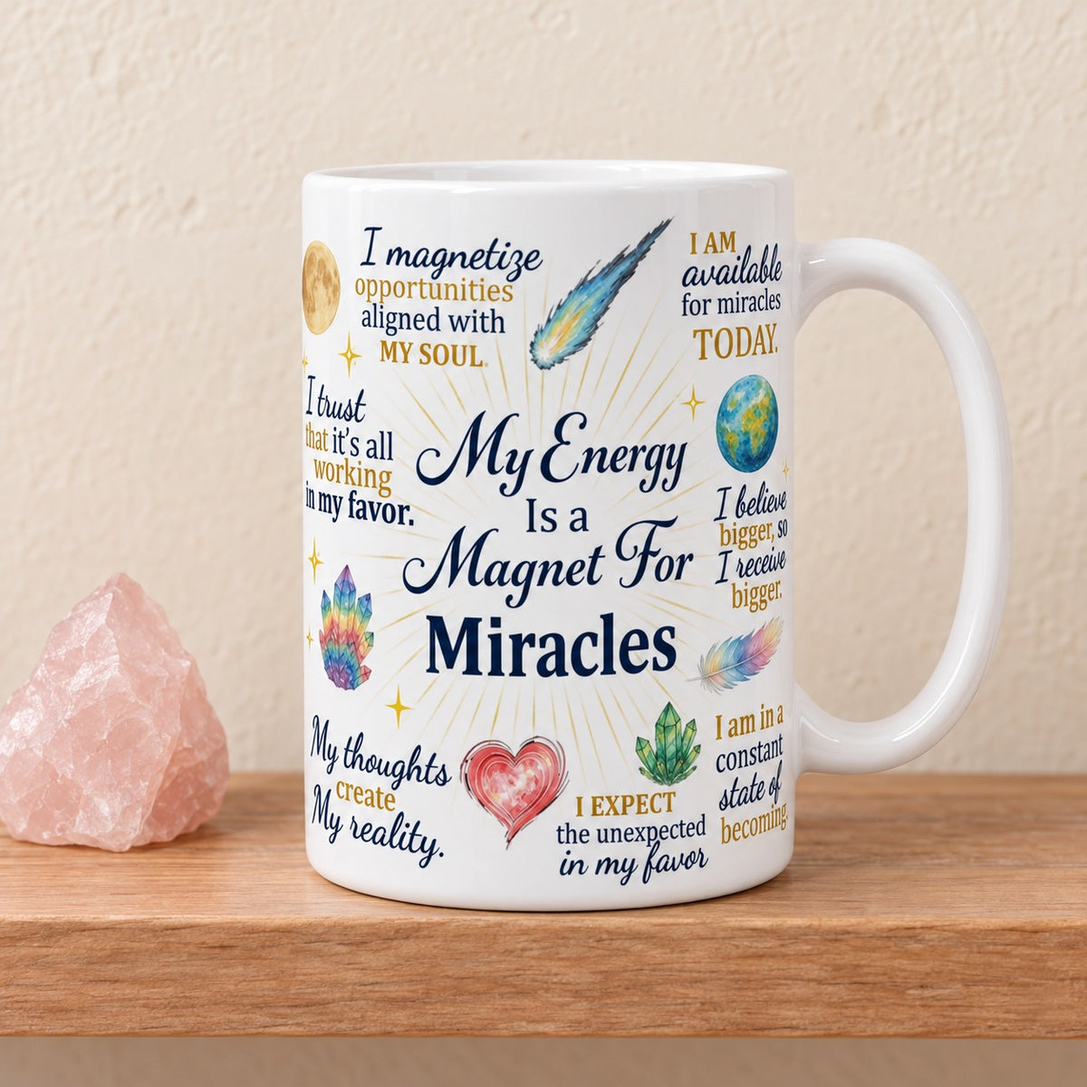 My Energy Is a Magnet For Miracles 15 oz white mug with the navy title facing forward among gold and navy affirmations, crystals and a comet, on a light oak shelf beside a rose quartz crystal