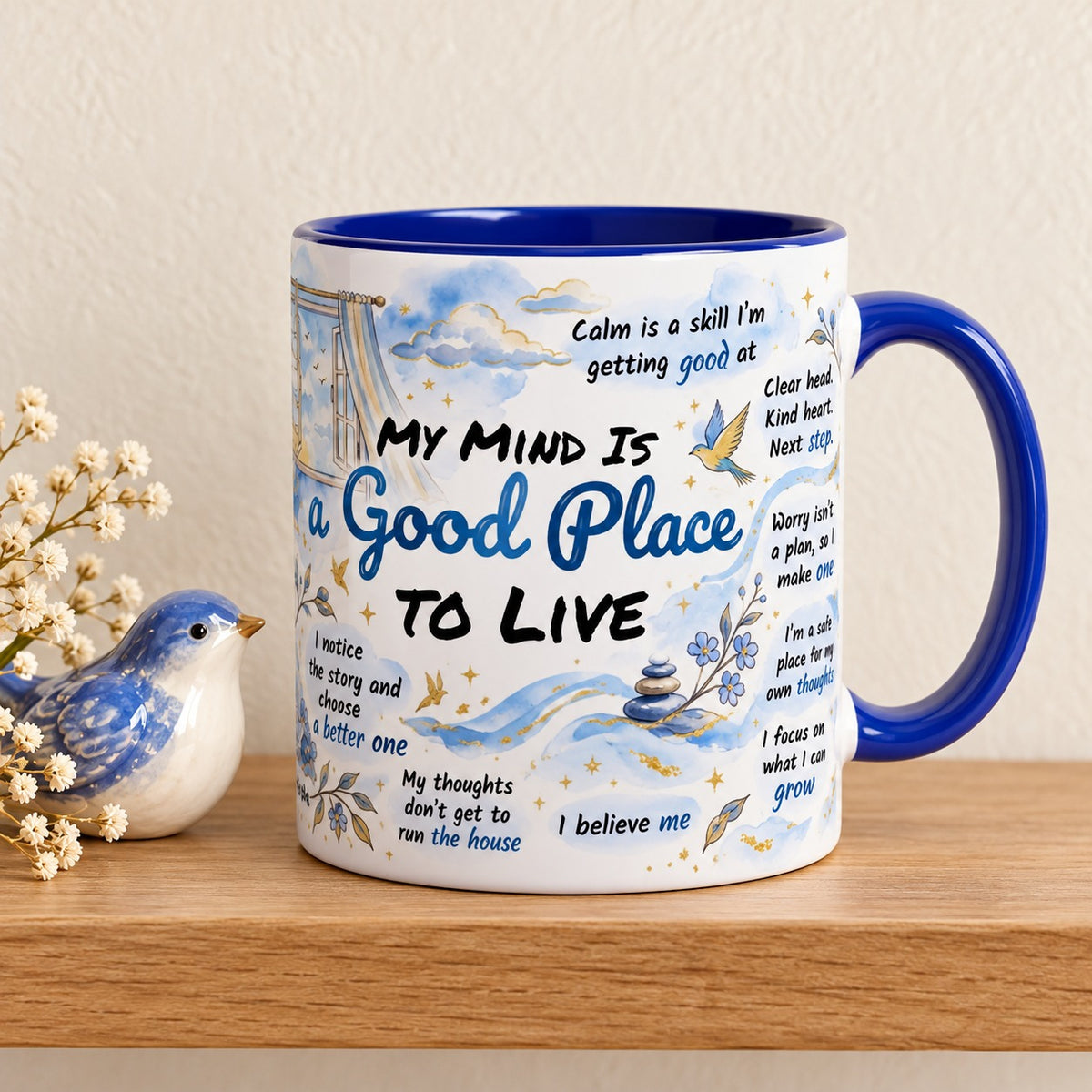 My Mind Is a Good Place to Live 11 oz mug with a blue handle and blue inside, title facing forward, resting on a light oak shelf beside a blue ceramic bird