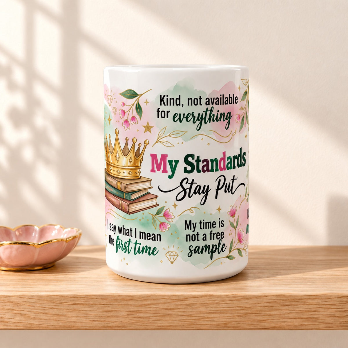 My Standards Stay Put 15 oz white mug with the title facing forward, resting on a light oak shelf beside a pink trinket dish