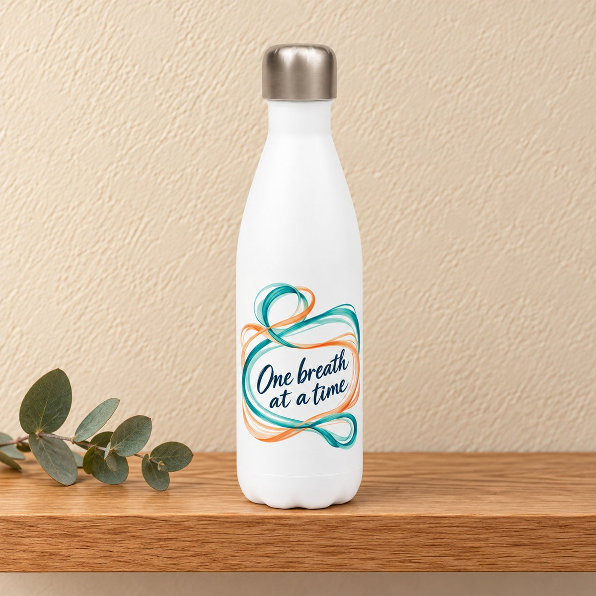 One Breath at a Time 17 oz white water bottle with teal and orange ribbons around navy script, standing on a light oak shelf beside a eucalyptus sprig