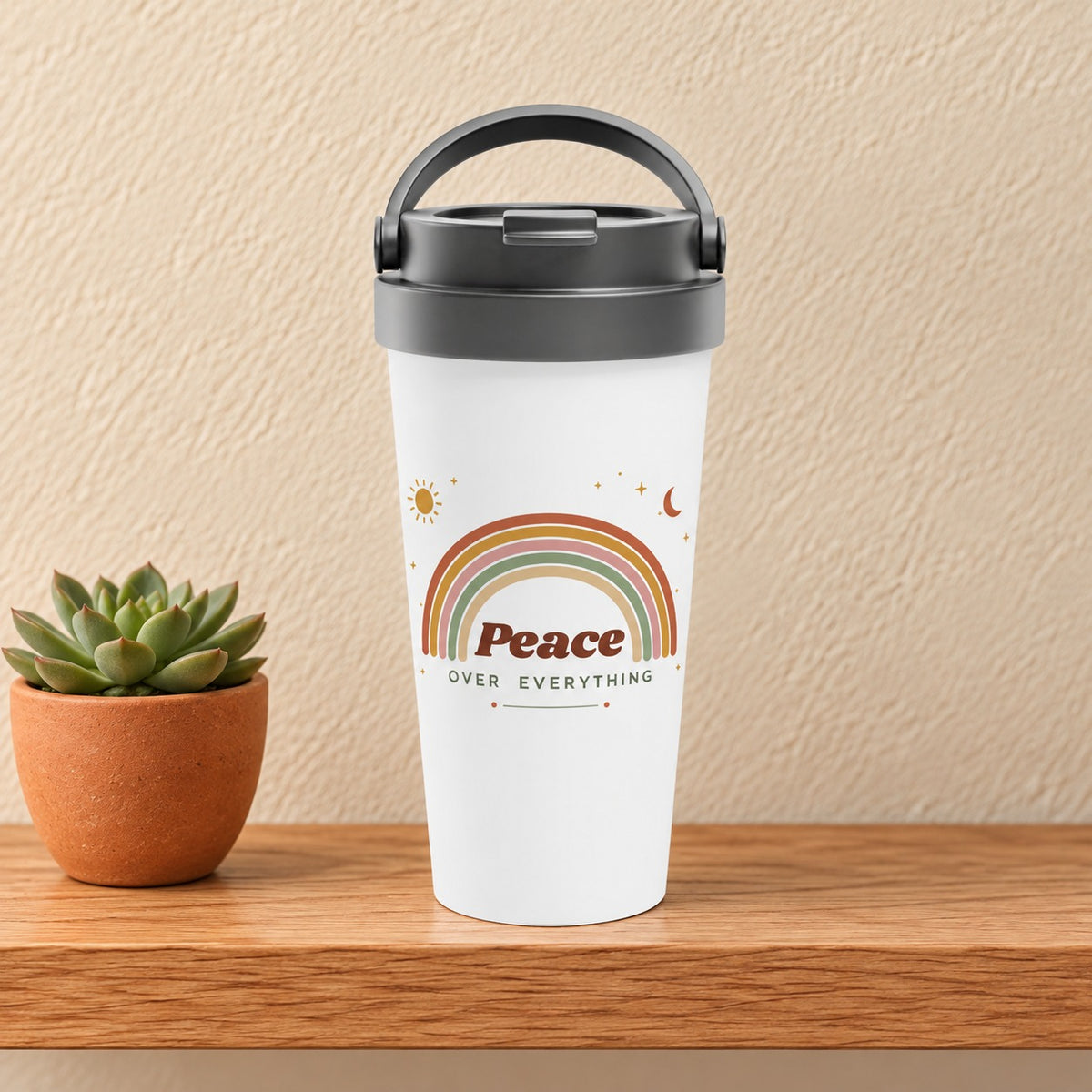 Peace Over Everything 15 oz white travel mug with a soft boho rainbow, sun and moon, standing on a light oak shelf beside a small succulent