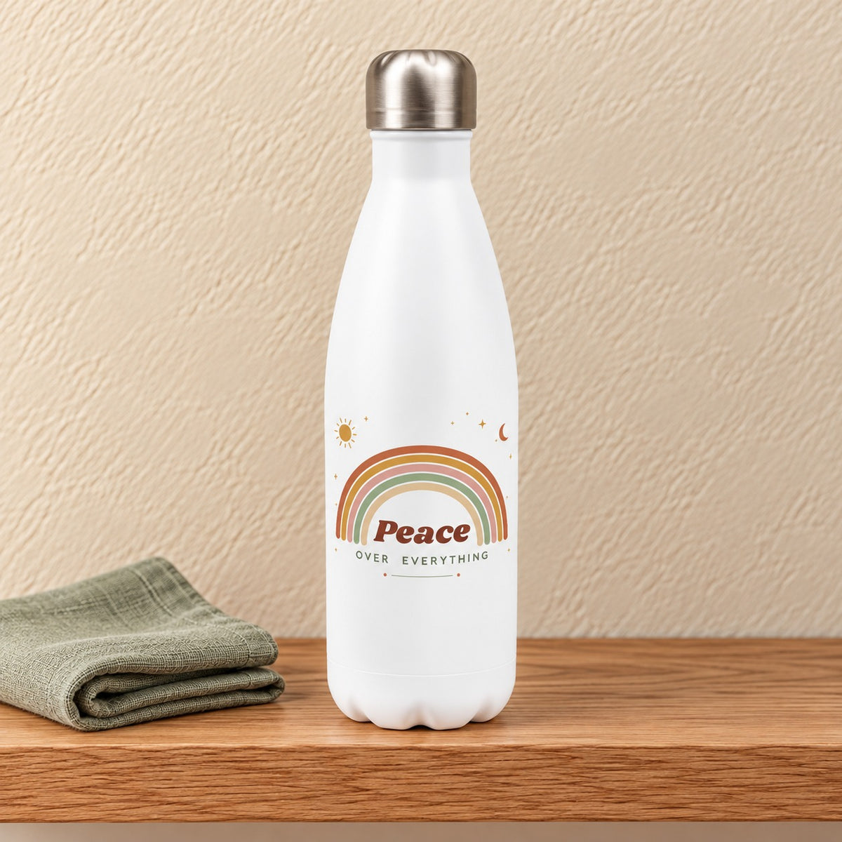 Peace Over Everything 17 oz white water bottle with a soft boho rainbow, sun and moon, standing on a light oak shelf beside a sage linen napkin