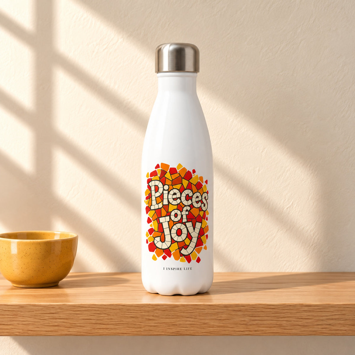 Pieces of Joy 17 oz white stainless steel water bottle on a light oak shelf beside a small yellow ceramic bowl, design facing forward