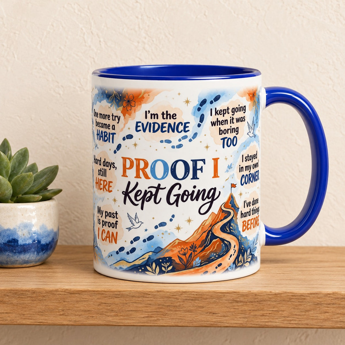 Proof I Kept Going 11 oz mug with a blue handle and blue inside, title facing forward, resting on a light oak shelf beside a small succulent