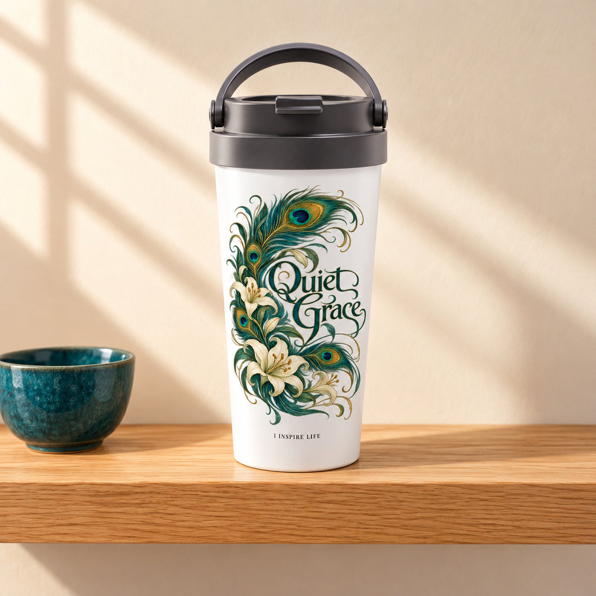 Quiet Grace 15 oz white stainless steel travel mug on a light oak shelf beside a small teal ceramic bowl, design facing forward