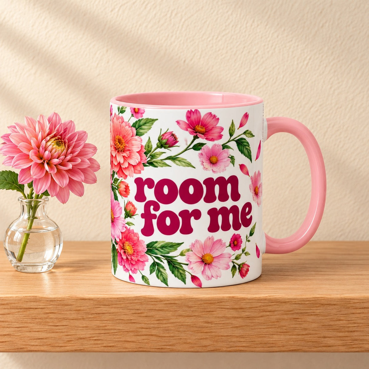 Room for Me 11 oz mug with a pink handle and pink inside, title facing forward among pink dahlias, resting on a light oak shelf beside a dahlia in a glass bud vase