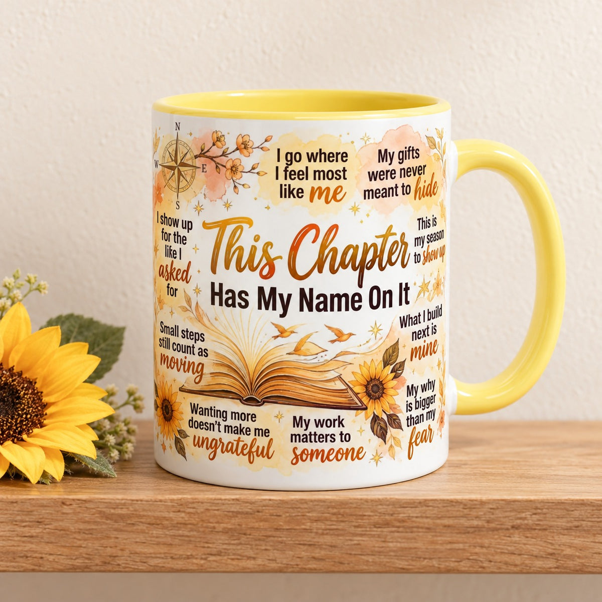 This Chapter Has My Name On It 11 oz mug with a yellow handle and yellow inside, title facing forward, resting on a light oak shelf beside a sunflower