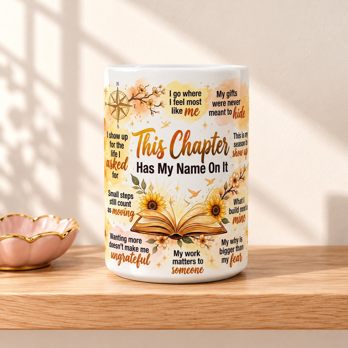 This Chapter Has My Name On It 15 oz white mug with the title facing forward, resting on a light oak shelf beside a small pink dish