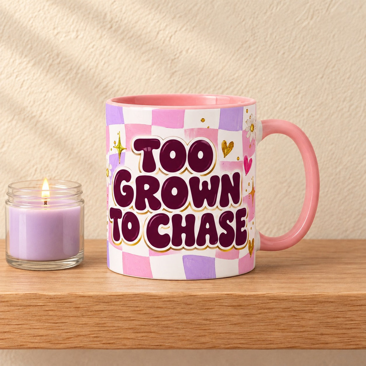 Too Grown to Chase 11 oz mug with a pink handle and pink inside, title facing forward on a pink and lilac checkerboard, resting on a light oak shelf beside a lilac candle