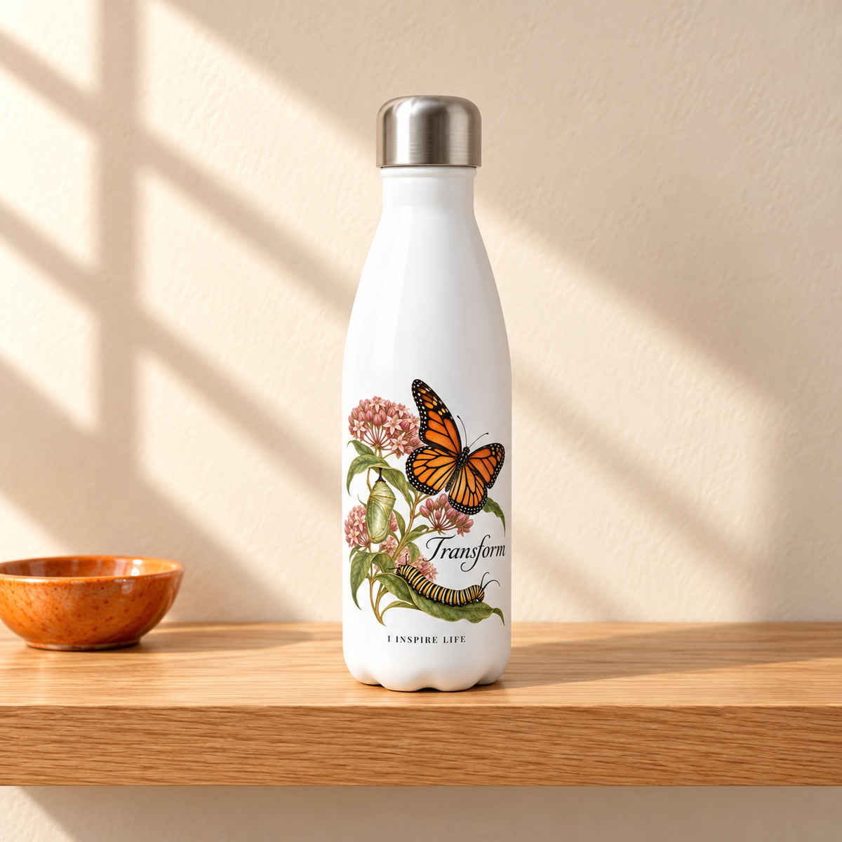 Transform 17 oz white stainless steel water bottle on a light oak shelf beside a small orange ceramic dish, design facing forward