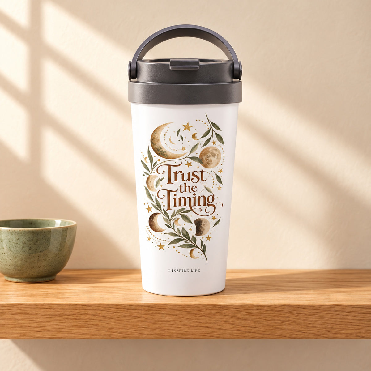 Trust the Timing 15 oz white stainless steel travel mug on a light oak shelf beside a small sage green ceramic bowl, design facing forward