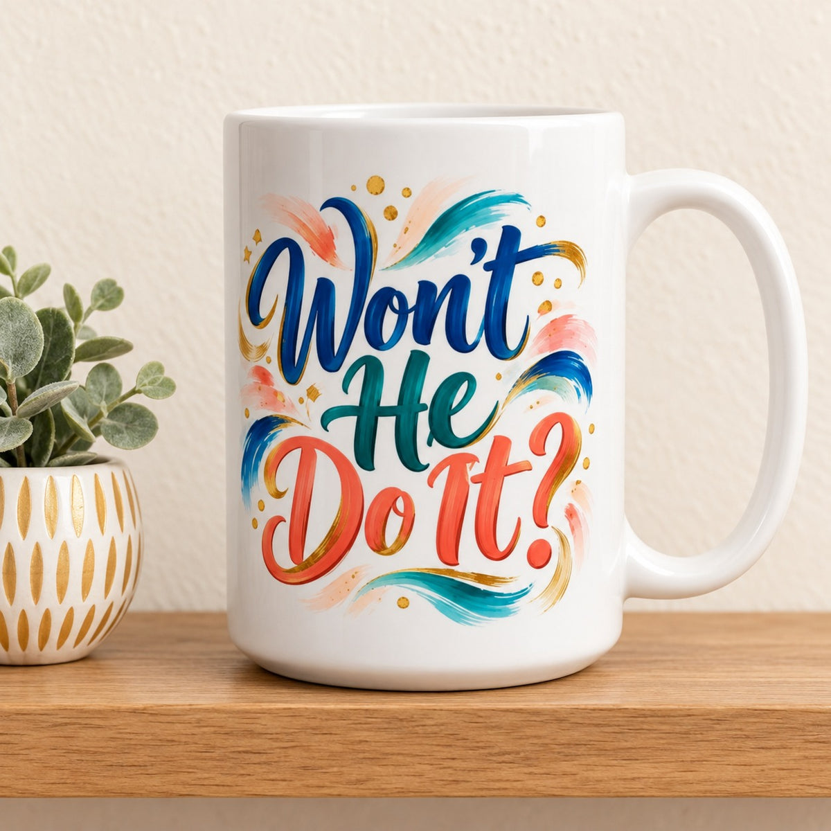 Won't He Do It? 15 oz white mug, front lettering facing forward, resting on a light oak shelf beside a small eucalyptus plant